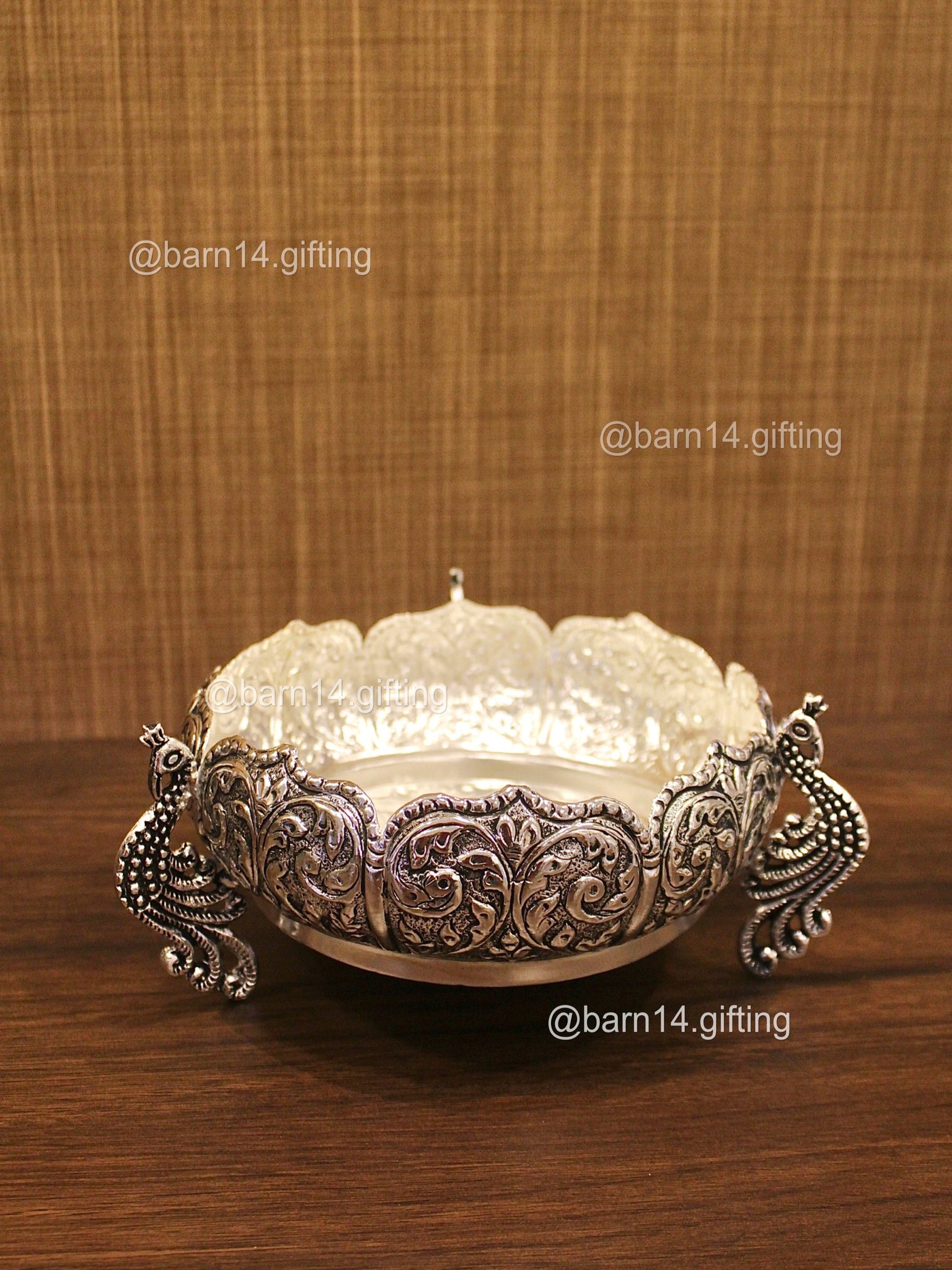 Decorative silver bowl with intricate designs on a wooden surface and brown textured background