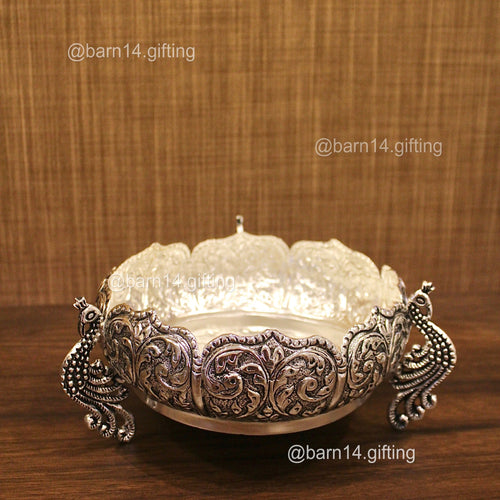 Decorative silver bowl with intricate designs on a wooden surface and brown textured background